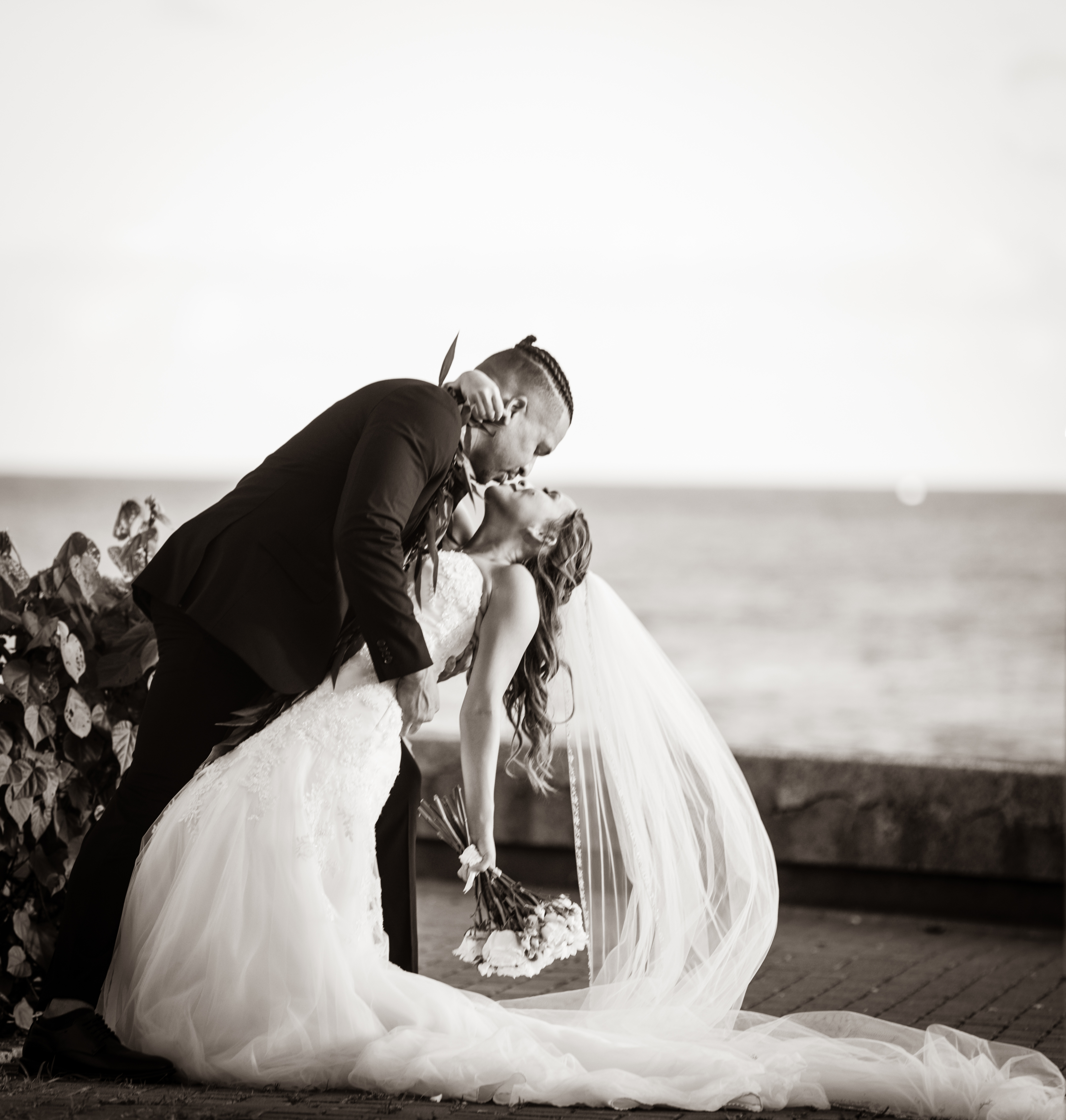 Pua and Kash share a kiss in their wedding clothes beside the ocean.